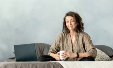 Genç esmer bir kadın kanepede otururken yatak odasında dizüstü bilgisayar kullanıyor. Film izlemek, arkadaşlarıyla sohbet etmek, kitap okumak ve e-postayı izlemek için dizüstü bilgisayar kullanıyor..