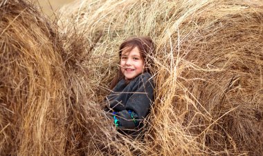 Samanlıkta oturan mutlu genç kız. Gülümsüyor ve eğleniyor..