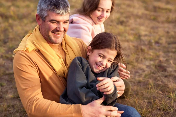 Happy dad and adult daughters having fun in the meadow outside at sunset. Happy man and little daughters spend time together. They\'re out for a walk. The family concept.