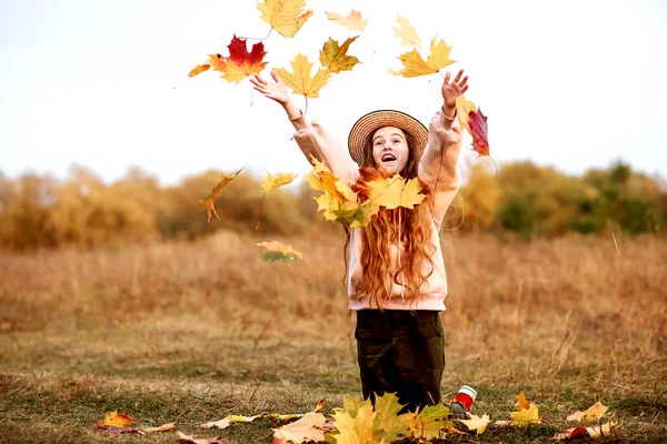 Feliz adolescente en un sombrero de paja lanza hojas de otoño. — Foto de Stock