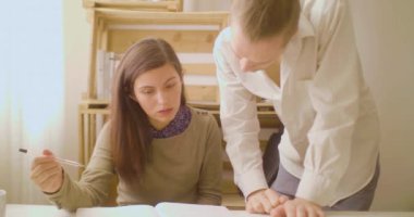 Masasında oturan genç İspanyol kadın yanında sarışın, beyaz bir adamla konuşuyor.