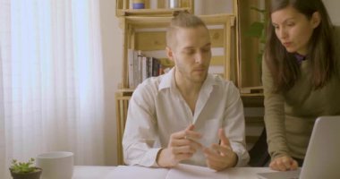 Masasında oturan sarışın, beyaz bir adam yanında genç bir İspanyol kadınla konuşuyor.