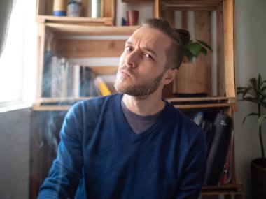 Pencerenin yanında sigara içen genç beyaz bir adam.