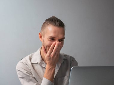 Kafkasyalı adam ağzını kapatıyor, bilgisayarın önünde gülümsüyor, Coronavirus salgını için karantinada görüntülü konuşuyor.