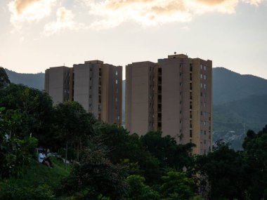 Medellin şehrinin manzarası, binalar, gün batımında dağlarla çevrili ağaçlar.
