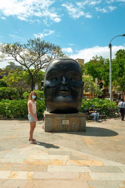 Medellin, Antioquia, Kolombiya - 6 Ocak 2021: Bronz bir heykelin önünde poz veren Kafkas Kız, Plaza Botero 'da Fernando Botero' nun bir Şişko Kafa Heykeli