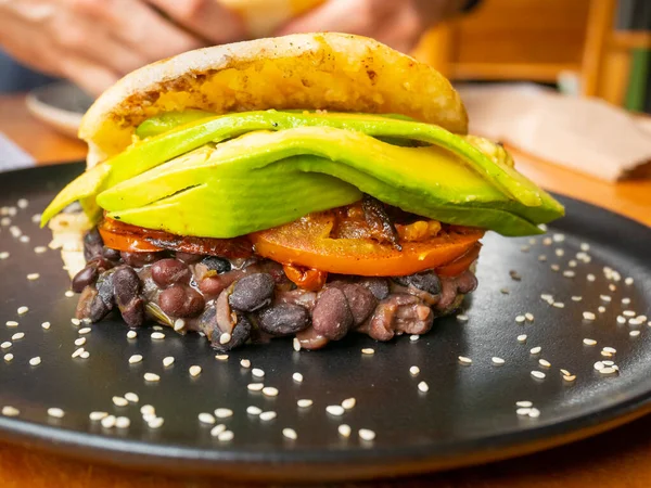 Tipik Venezuela Atıştırmalık Arepa Kara Fasulye ile doldurulmuş Kurutulmuş Domates ve Avokado Siyah Tabakta