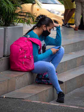 Itagui, Antioquia, Kolombiya - 7 Mart 2021: Genç İspanyol Maskeli Kadın Merdivenlerde Oturuyor ve Telefonunda Sohbet Ediyor