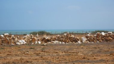 Punta Gallinas, Uribia, La Guajira, Kolombiya 'da okyanusun yanındaki tahta sopalı bir Çit yakınındaki Taşlardan yapılmış Duvar ile Kuru Kum Toprağı