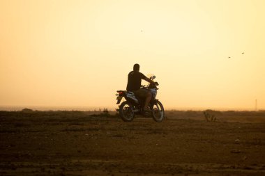 Uribia, La Guajira, Kolombiya - 28 Mayıs 2021: Gündoğumu Güneşi Işıklarında Sarı Arkaplan ile Motosiklete Binen Latin Adam