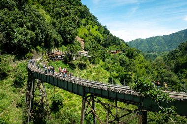 Amaga, Antioquia, Kolombiya - 18 Temmuz 2021: Güneşli bir günde Ağaçlarla dolu Bir Ormanın Ortasında Eski Kırsal Demiryolu Köprüsü 'nde Çok sayıda Turist Yürüyor