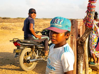 Uribia, La Guajira, Kolombiya - 27 Mayıs 2021: Küçük Wayuu Çocuk El Yapımı El Sanatları ve Motosikletli Bir Genç Adam Kameraya Bakıyor ve Gülümsüyor