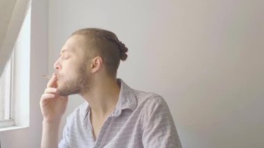 Gri gömlekli beyaz adam Medellin, Kolombiya 'daki Beyaz Oda' da Pencerenin önünde sigara içiyor.