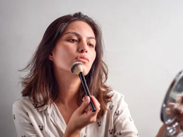 Young Beauty Brown Hair Peruvian Woman Applies Make Up with a Brush Looking at Herself in a Small Round Mirror
