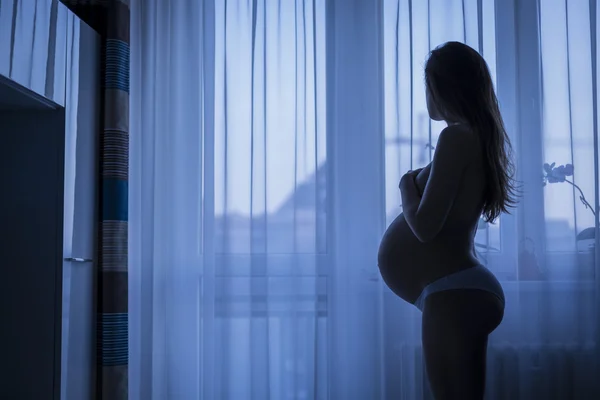 Femme enceinte regardant par la fenêtre — Photo