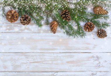 Kar çerçeveli beyaz ahşap bir zemin üzerinde köknar dalları ve konilerin noel arkaplanı.