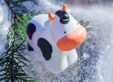 Bir ineğin plastik heykeli ve buzdaki bir köknar dalı.