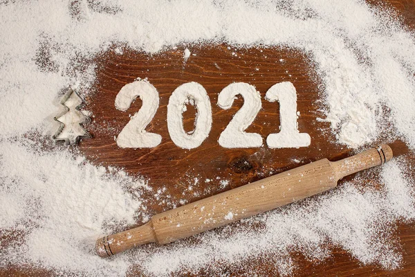 2021 yazıtları ahşap bir masanın üzerindeki undan yapılmış, etrafa beyaz un saçılmış ve yuvarlak bir iğne var.