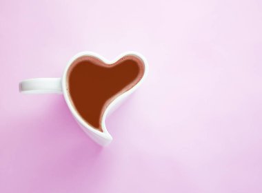 Bir adet pembe arka planda kahve ya da sıcak çikolata kaplı kalp şeklinde seramik beyaz bardak, fotokopi alanı olan üst manzara.