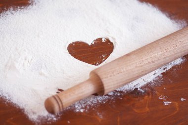 Tahta masaya bir kalp ve merdane serpiştirilmiş un serpiştirilmiş.