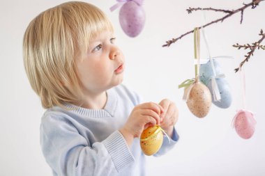 Çocuk, ağaç dallarını renkli yumurta şeklinde Paskalya süslemeleriyle süslüyor.