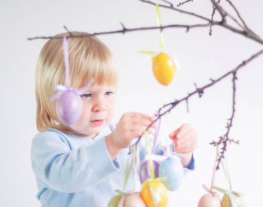 Çocuk dekoratif paskalya yumurtalarını arka plandaki ağaç dallarına asıyor.