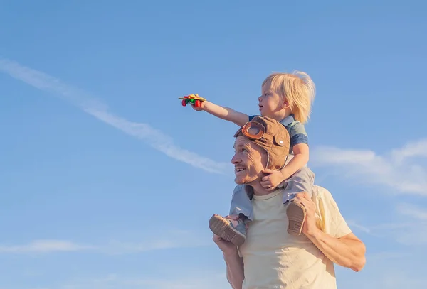 Küçük çocuk dışarıda babasının omuzlarında otururken oyuncak bir uçakla oynuyor.