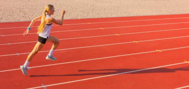 Spor üniformalı genç sarışın kadın spor stadyumunda koşuda hızlı koşar. Spor eğitimi ve egzersiz, sağlıklı yaşam tarzı..