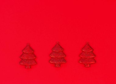 Kırmızı arka planda üç kırmızı dekoratif Noel ağacı ve fotokopi alanı. Noel ve Yeni Yıl tatillerinin minimalist kompozisyonu.