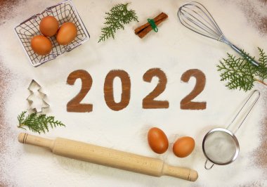 2022 numara, mutfak aletleri ve tavuk yumurtalarının ortasındaki ahşap bir masanın üzerindeki un üzerinde. yeni yıl konsepti.
