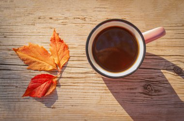 Güneşli bir günde, sonbahar yapraklarının yanında, ahşap bir masada sıcak içecekle sıcak bir fincan.