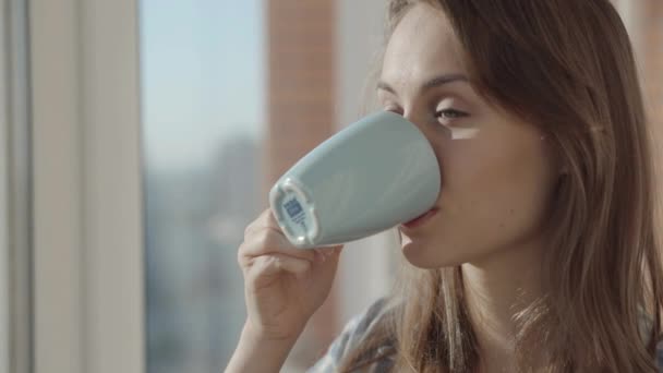 Женщина пьет кофе у окна — стоковое видео