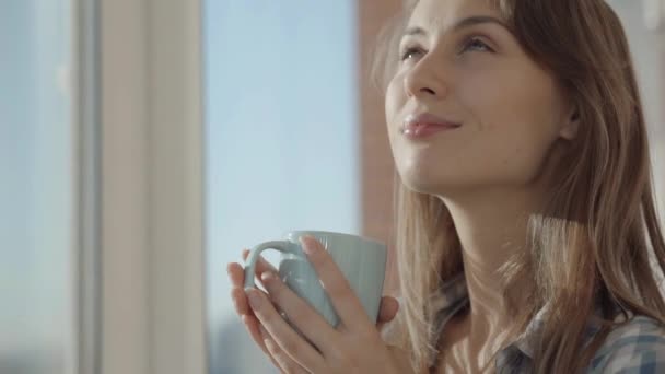 Kvinna dricker kaffe vid fönstret — Stockvideo