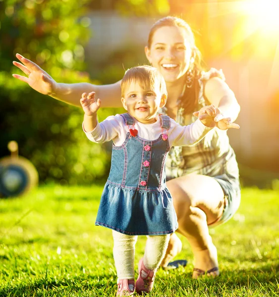 Bebé niña está haciendo sus primeros pasos con las madres ayudan — Foto de Stock