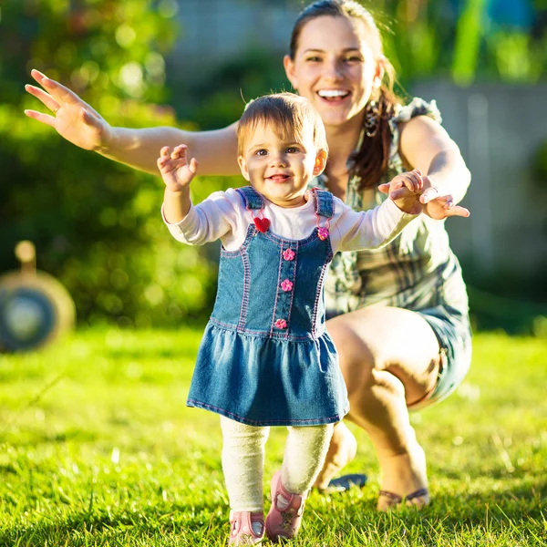 Bebé niña está haciendo sus primeros pasos con las madres ayudan — Foto de Stock