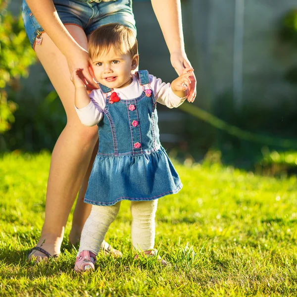 Bebé niña está haciendo sus primeros pasos con las madres ayudan — Foto de Stock