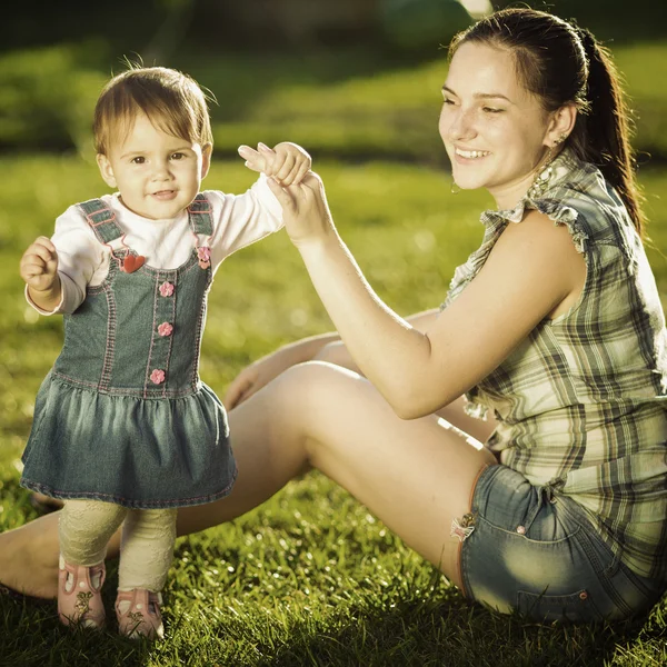 Vauva tyttö tekee hänen ensimmäiset askeleensa äitien kanssa auttaa — kuvapankkivalokuva