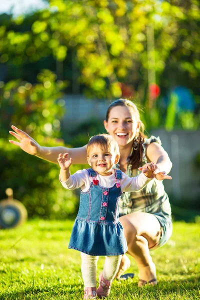 Bebé niña está haciendo sus primeros pasos con las madres ayudan — Foto de Stock