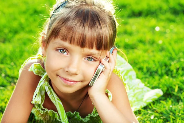 Liten flicka prata telefon och liggande på gräs — Stockfoto