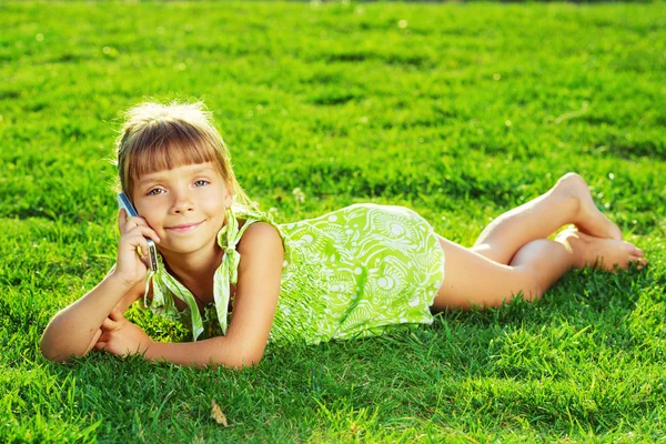 Malá holčička mluví telefonu a ležící na trávě — Stock fotografie