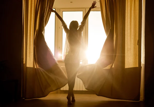 Γυναίκα κοιτάζοντας την Ανατολή του ηλίου στέκεται κοντά σε παράθυρο — Φωτογραφία Αρχείου