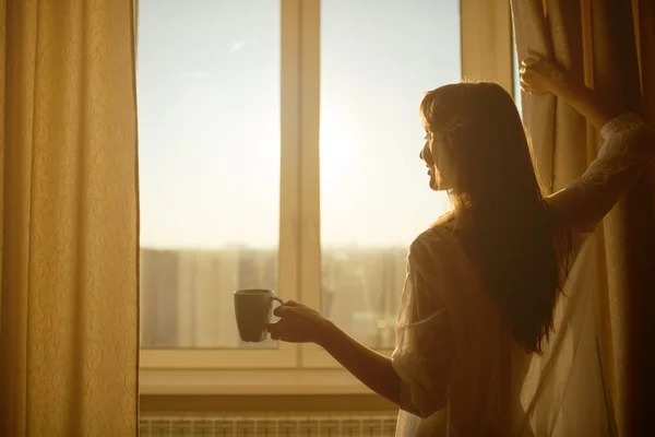 Mulher segurando xícara de chá e olhando para o nascer do sol — Fotografia de Stock
