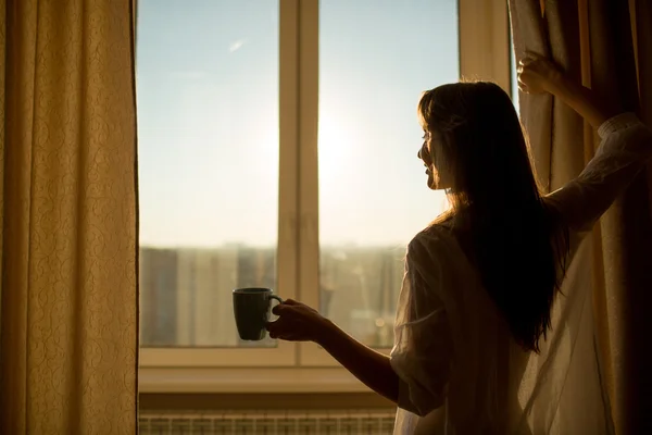 Çay tutarak ve güneş doğarken arayan kadın