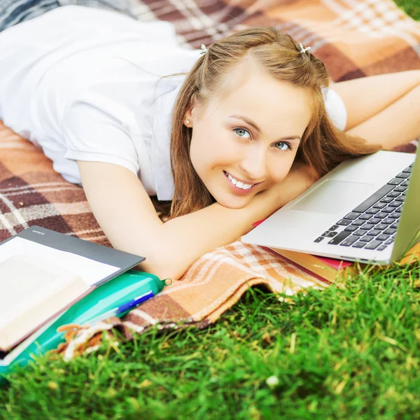 Student vrouw liggen op het gras met laptop — Stockfoto