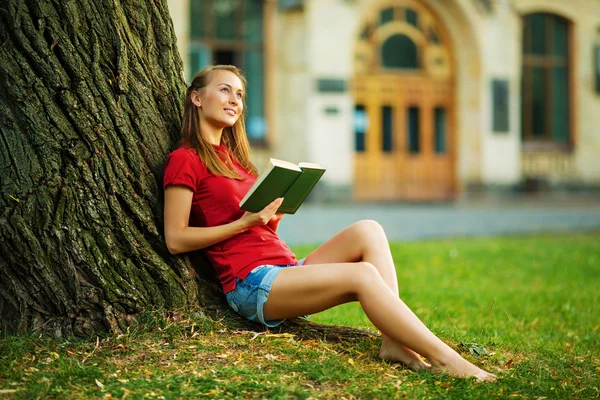 Étudiante assise près d'un arbre avec livre — Photo