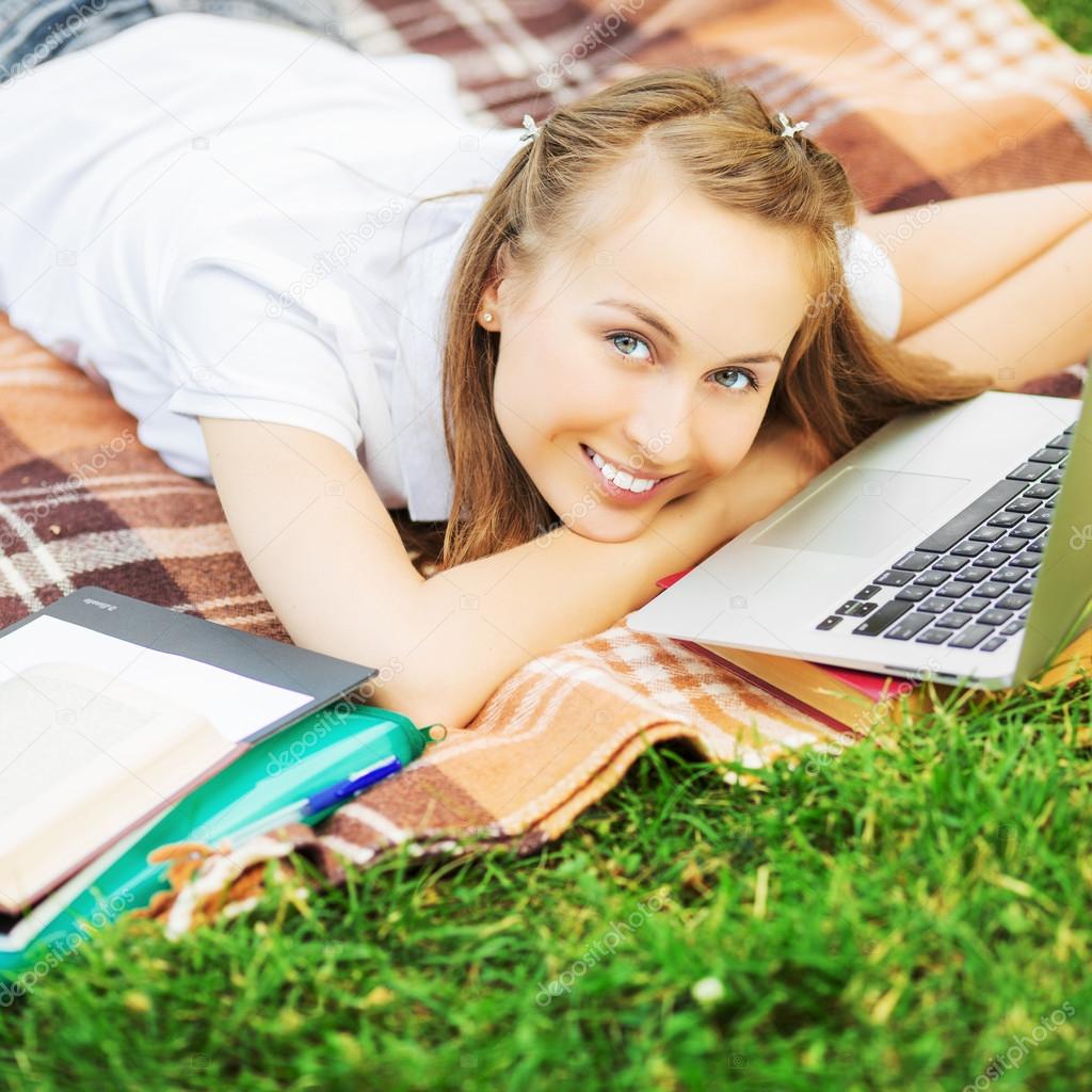 Student woman lying on the grass with  laptop