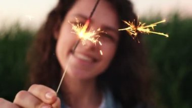 Genç bir kadın elinde maytap tutuyor, seçici bir odak noktası. Noel 'i dışarıda kutluyor, yeni yıl arifesinde bağımsızlık gününün tadını çıkarıyor. Havai fişekler, Bengal ışıkları ağır çekimde.