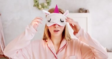 Genç esneyen pembe pijamalı ve uyku maskeli bir kadın, uyanıp uykusundan sonra geriniyor, uykulu ve mutlu. İyi ve sağlıklı uyku konsepti.