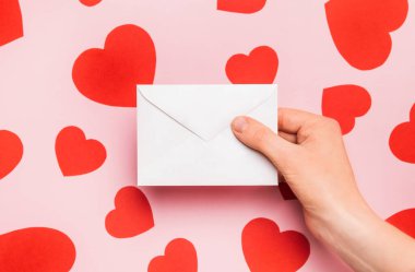 Sevgililer günü için beyaz zarf mektup, aşk ilanı. Soluk pembe arka planda sevgililer günü için kırmızı kalplerle kompozisyon. Düz yatıyordu. Aşk ve ilişkiler kavramı.