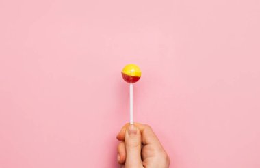 Renkli lolipop şeker çubuğu elinde. Pembe arka planda çilekli muz tatlısı. 